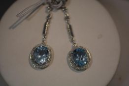 A striking pair of aquamarine and diamond drop earrings, each with an oval-cut aquamarine claw set