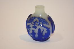 A Chinese glass snuff bottle of Peking type, the blue overlay over a milky white ground, carved with