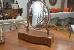 A George III style mahogany toilet mirror, the oval plate over a serpentine platform fitted with