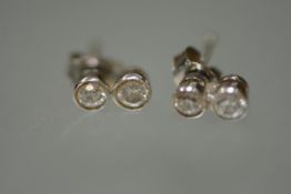 A pair of two-stone diamond ear studs, each with two graduated stones collet set, in white metal,