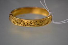 A late Victorian gold (unmarked) hinged bangle, one half pierced with a grape and vine leaf pattern,