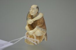 A Japanese ivory netsuke carved as a street vendor, a basket at his feet, holding a scoop, two