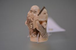 A Japanese ivory netsuke, carved as a man and a child playing with a mask, inscribed to the base.