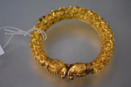 An Indian yellow metal hinged bangle, probably high carat gold, with exotic beast terminals, the