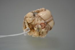 A Japanese ivory netsuke, carved as a crouching vendor under the weight of a large sack, decorated