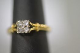A five stone diamond cluster ring, four round brilliants in a square setting centred by a smaller
