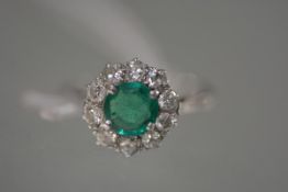 A vintage emerald and diamond cluster ring, the round-cut emerald claw set within a band of ten