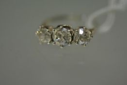 A three stone diamond ring, the graduated round brilliants claw-set on a white metal band, unmarked,