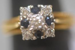 A diamond and sapphire cluster ring, the central round brilliant-cut diamond claw-set above a square