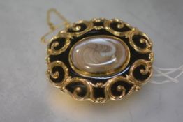 An early Victorian gold (unmarked) and black enamel mourning brooch pendant, oval, centred by a