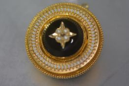 A Victorian mourning brooch in the Etruscan taste, of circular form, the central black glass panel