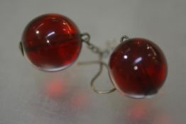 A pair of cherry amber drop earrings, each spherical bead suspended from a white metal chain, fish