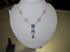 A striking blue topaz and diamond pendant, designed as twin flowerheads spaced by diamond-set hoops,