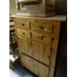 A tall honey pine chest comprising four small drawers above a pair of two-door cupboards together