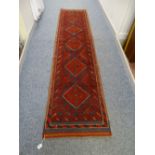 A HAND KNOTTED WOOL MESHWANI RUNNER CARPET, predominantly red ground with central repeating