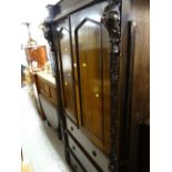 An early twentieth century oak press cupboard with three drawers & profuse carving to the side