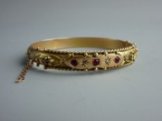 A NINE CARAT GOLD DIAMOND & RED STONE SET BANGLE with bead and rope decoration with floral shoulders