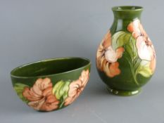 A MOORCROFT 'HIBISCUS' 19 cms HIGH BALUSTER VASE and an oval vase, both decorated on a green ground,