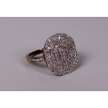 A DIAMOND CLUSTER RING the diamonds in an oval with diamonds to the shoulders set to 9ct yellow gold