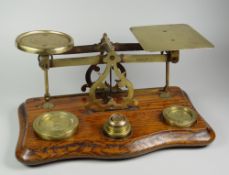 A SET OF ANTIQUE BRASS POSTAL-SCALES on a shaped oak base with six various disc weights, the