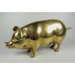 A BRASS MONEY BOX in the form of a standing pig, with loop tail and coin slot, 27cms high