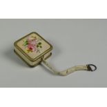 A GUILLOCHE ENAMEL-TYPE DRESS-MAKER'S TAPE-MEASURE with pretty rose decoration to the top and return