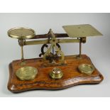 A SET OF ANTIQUE BRASS POSTAL-SCALES on a shaped oak base with six various disc weights, the