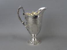 A SILVER HELMET SHAPED JUG with leaf cast handle, pedestal circular base and chased decoration,