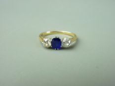 AN UNMARKED GOLD DRESS RING with blue oval central stone and two quarter carat flanking diamonds,