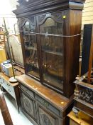 An early twentieth century bookcase-cupboard with carving to the door friezes & with brass handles