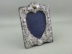 A SILVER EASEL PORTRAIT FRAME, the heart shaped reveal surrounded by cherubic floral and latticed