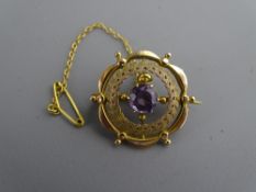 AN UNMARKED GOLD 'SHIP'S WHEEL' BROOCH having a centre purple stone with surrounding wreath, 3