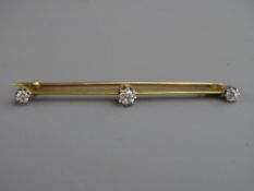 AN UNMARKED GOLD BAR BROOCH having a centre diamond, approximately 0.25 carat and two smaller end