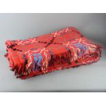 A RED WELSH WOOLLEN BLANKET in traditional multi-coloured design with tasselled edges, 240 x 210 cms