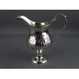 A CLASSICALLY STYLED SILVER PEDESTAL CREAM JUG with embossed floral decoration and gilt interior,