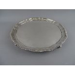 A LARGE CIRCULAR SILVER SALVER with wavy edge and gadrooned border on four gripping hand feet,