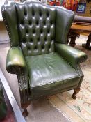 A VINTAGE GREEN LEATHER EFFECT WINGBACK ARMCHAIR with button back upholstery, 105 cms high, 80 cms