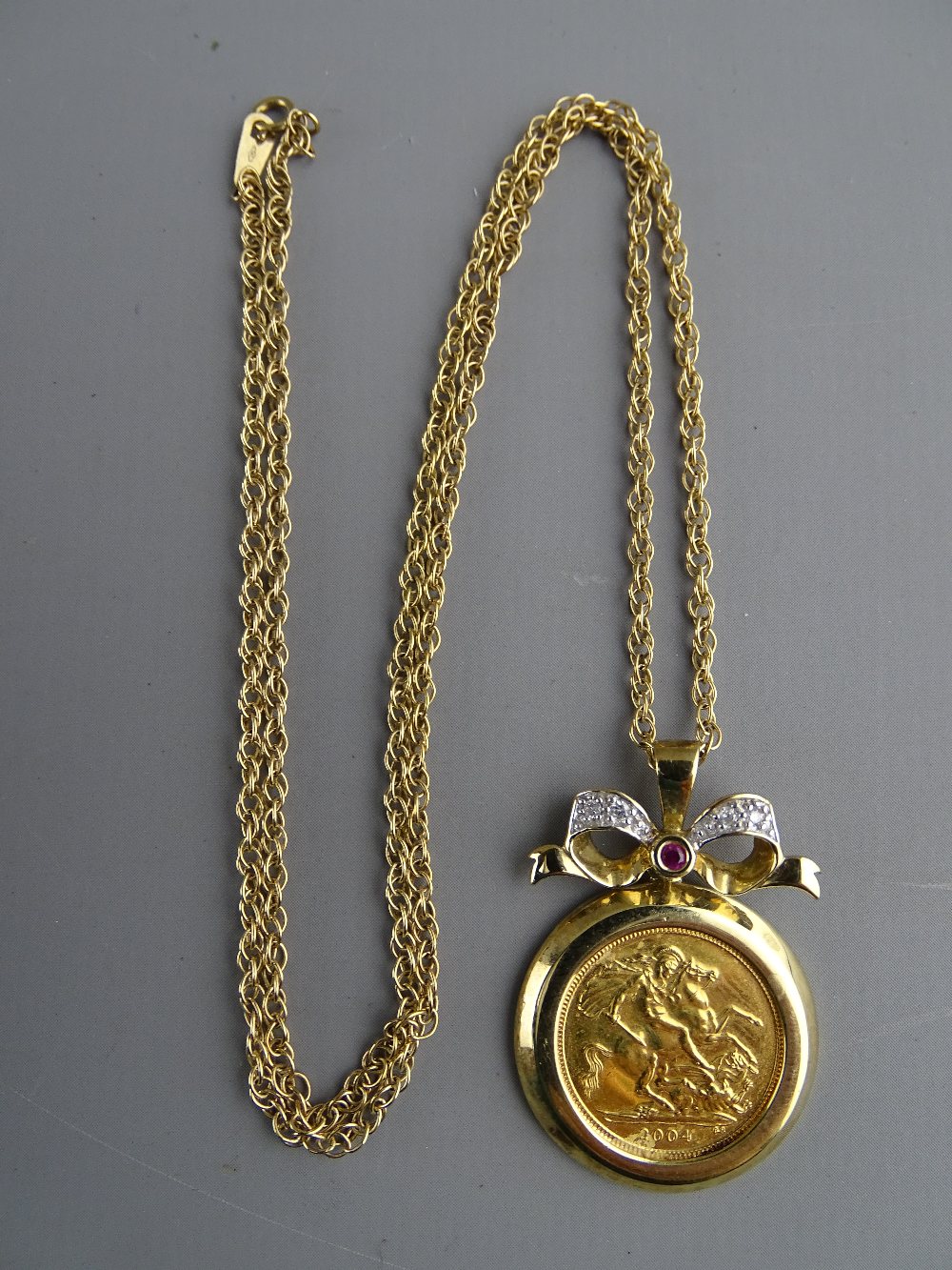 A NINE CARAT GOLD NECK CHAIN with decorative bow link to a gold mounted half sovereign 2004, total