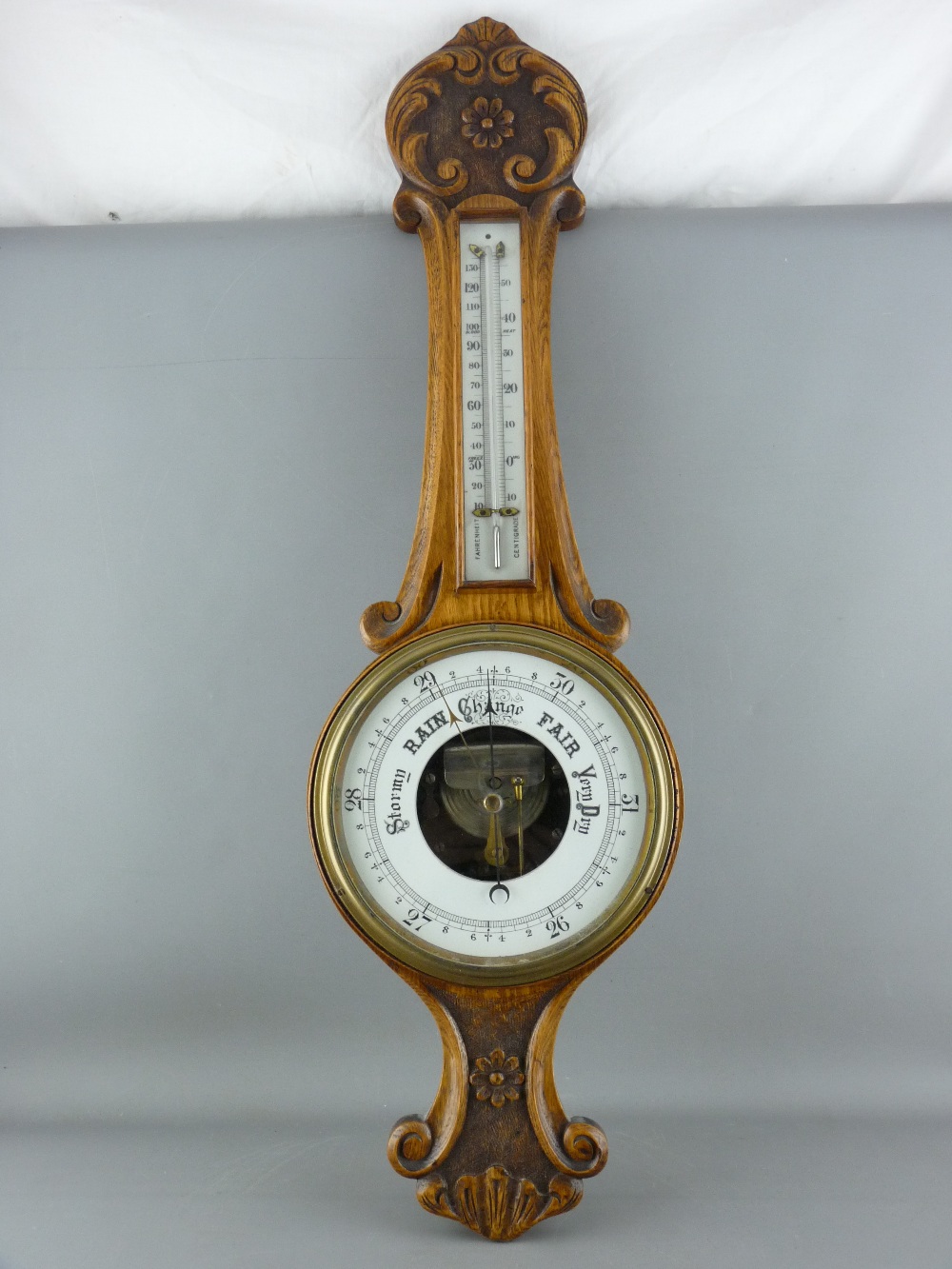 A CARVED OAK BANJO WALL BAROMETER with thermometer, 82 cms long