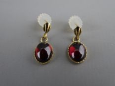 A PAIR OF NINE CARAT GOLD MOUNTED OVAL CABOCHON GARNET EARRINGS, total 1.2 grms