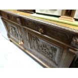 A substantial antique carved sideboard with two doors bearing carved panels of raucous tavern
