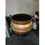 A copper coal bucket with copper handles standing on three feet