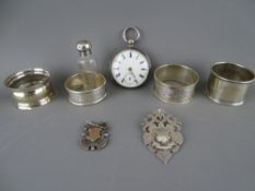 Silver cased pocket watch, two pendant fobs, four napkin rings and a screw top glass scent bottle,
