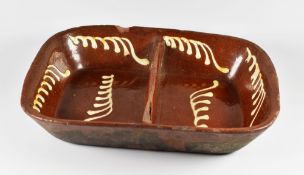 A SLIPWARE BAKING DISH OF TWO SECTIONS decorated with cream slip leaves, believed 19th Century,
