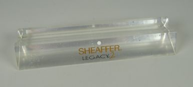 A CLEAR MOULDED PLASTIC STAND WITH SHEAFFER LEGACY 2 IMPRINT with protective film attached to base