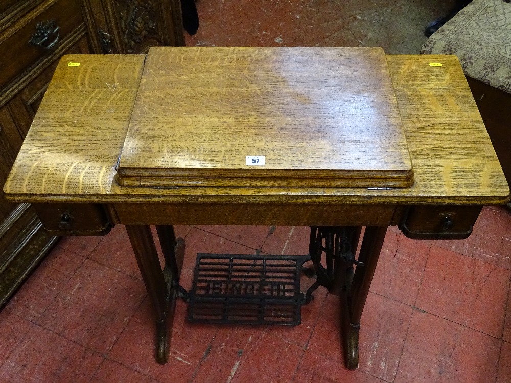 A SINGER TREADLE SEWING MACHINE in an oak fold-out work table, 77.5 cms high, 87 cms wide, 41.5