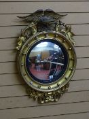 A REGENCY STYLE GILT CONVEX WALL MIRROR with eagle cresting and ball detail, 81 cms long overall, 53