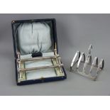 A CASED PAIR OF SILVER KNIFE RESTS and a four section silver toast rack, Birmingham 1900 and 1937