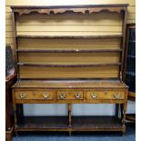 An antique oak Welsh dresser having a planked platform base, three drawers, an open rack with carved