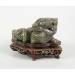 CHINESE SPINACH JADE STUDY OF A RECUMBENT LION DOG raised on carved hardwood base, 8cms high